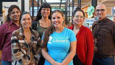 Six members of the Indigenous team inside a library standing with each other smiling