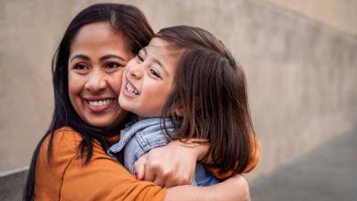 Mother hugs daughter tightly, they both are smiling.