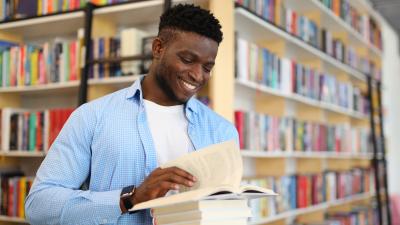 A person reads books in front of a bookshelf.