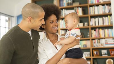 A multiracial family smiles at each other in front of bookshelves.