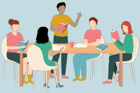 Four people seated around a table reading books, while a man in a yellow shirt stands up reading aloud from a book 