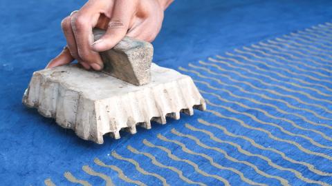 Photo of a person stamping a wavy kente print pattern on a blue fabric.