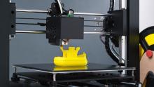 Photo of a 3D printer making a yellow toy boat.