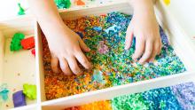 A photo of a child's hands in a sensory bin with rainbow colored rice.