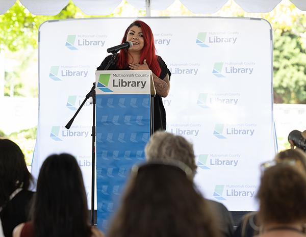 Woman standing behind a podium with a microphone looking towards an audience.