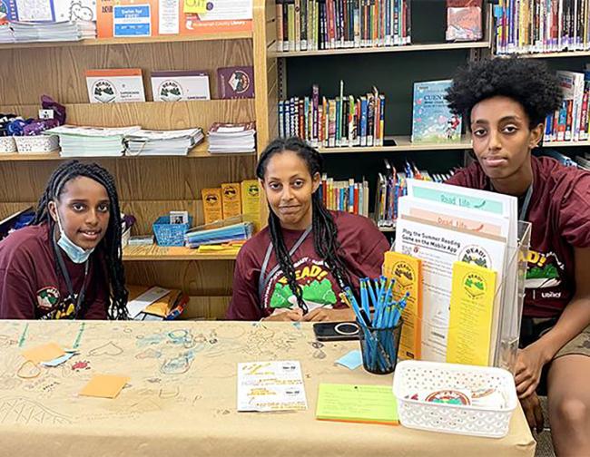 Three teen volunteers seated at a Summer Reading table in the library