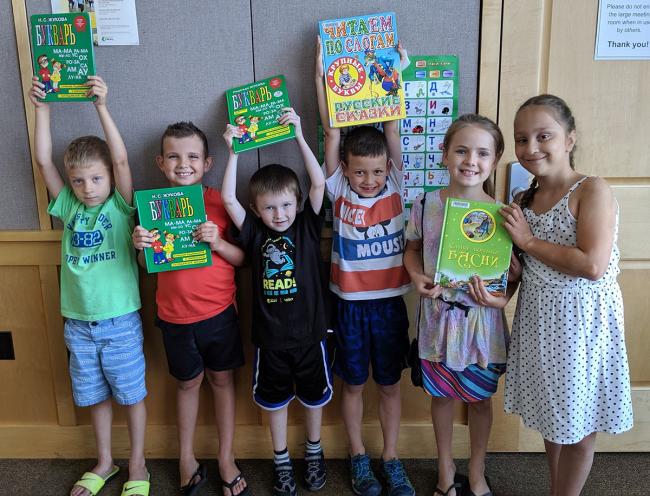 Kids from the Russian book club, inside the library standing with books in their hands.