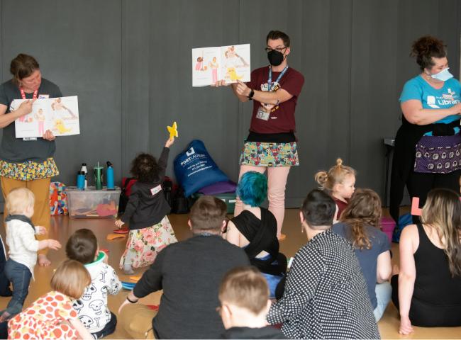 Three staff members standing each holding a book, people sitting watching them