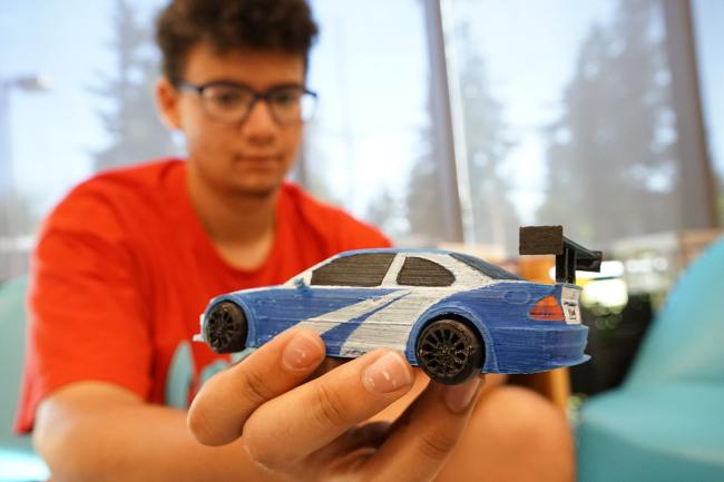 Adolescente en el Taller Creativo de Rockwood sosteniendo con su mano un carro creado con una impresora 3D.