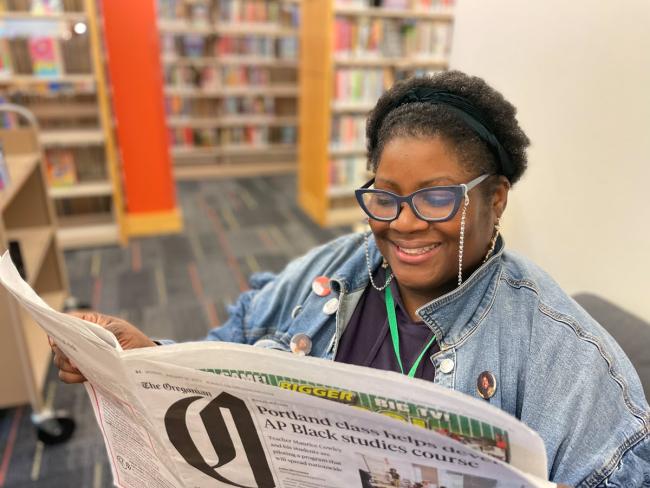 Woman sitting inside the library on a chair reading a newspaper