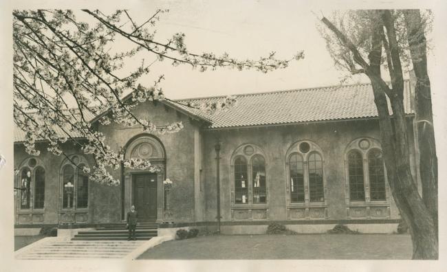 Historic photo of the exterior of the Albina Library Branch, a man in a suit is standing on the front steps.