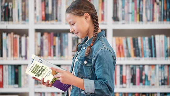 A young girl at the library with a book open in her hands