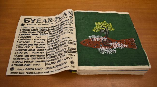 large format fabric book with list of participating artists on left side and painting of a tree on the right.