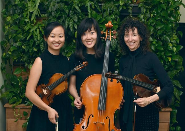 Three women standing with instruments, a violin a cello and a viola.