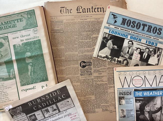 Newspaper issues of Willamette Bridge, The Lantern, Nosotros, Burnside Cadillac and Progressive Woman newspapers, laid out on a table on top of each other.